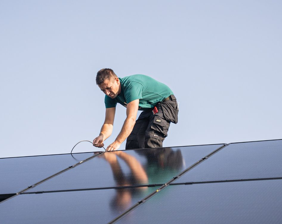 Person ist auf dem Dach und verkabelt Solarpanele